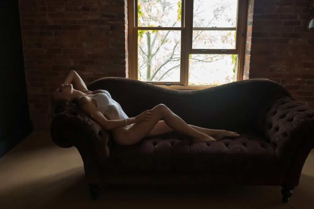 Woman in white body suite lying on couch during a boudoir suite.