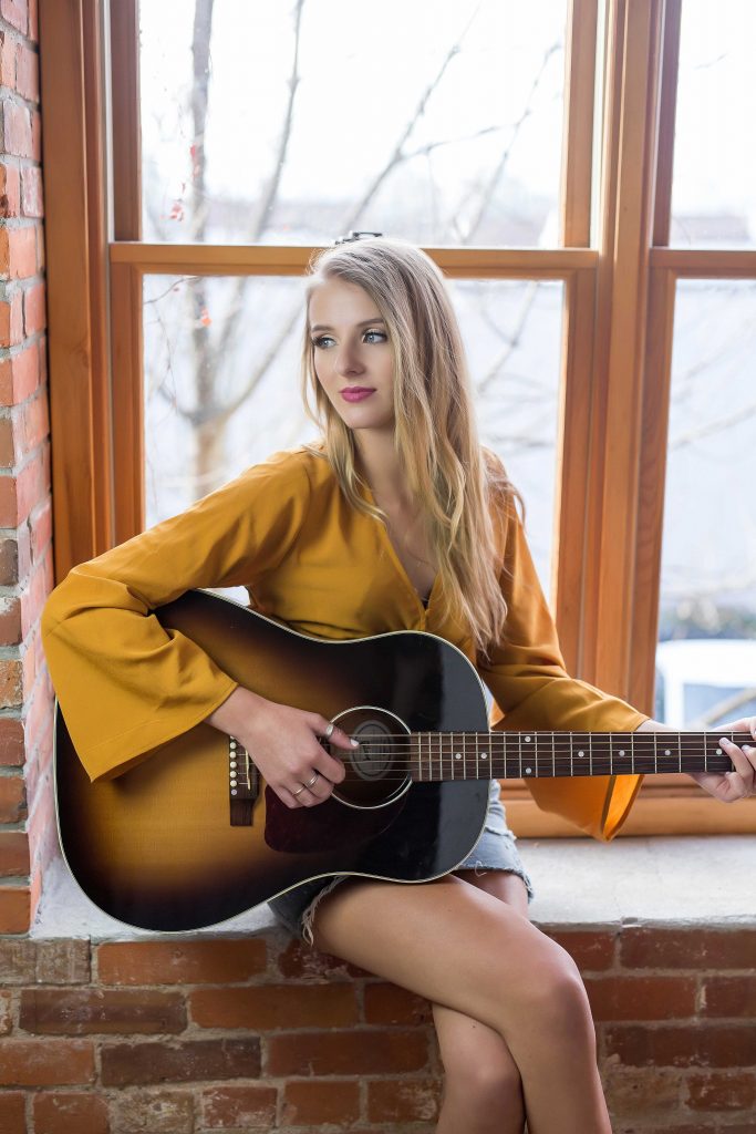 Girl plays guitar in yellow shirt.