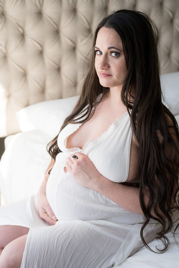 woman in white gown posing on bed for maternity shoot